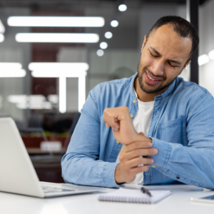 Man with carpal tunnel syndrome sitting at an office desk holding wrist in pain
